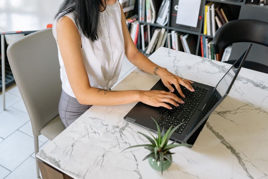 Mujer profesional escribiendo en una laptop en un entorno de oficina con una mesa de mármol moderna.