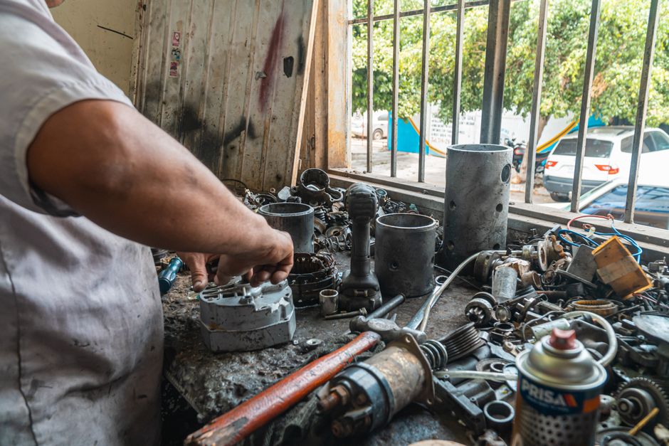 Mecánico organizando piezas en un taller activo, rodeado de herramientas y equipo.